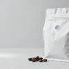 Unbranded stand-up coffee bean pouch with a one-way degassing valve and matte printed film, whole roasted coffee beans beside it