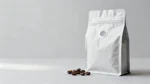 Unbranded stand-up coffee bean pouch with a one-way degassing valve and matte printed film, whole roasted coffee beans beside it