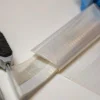三片厚度不同的软包装复合膜样品在白色台面上，用数显测厚仪逐片测量的特写