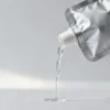an unbranded spout pouch with a screw cap, tilted mid-pour with a clear liquid stream, studio background